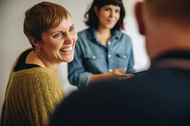 Two women smiling and talking in a group setting.
