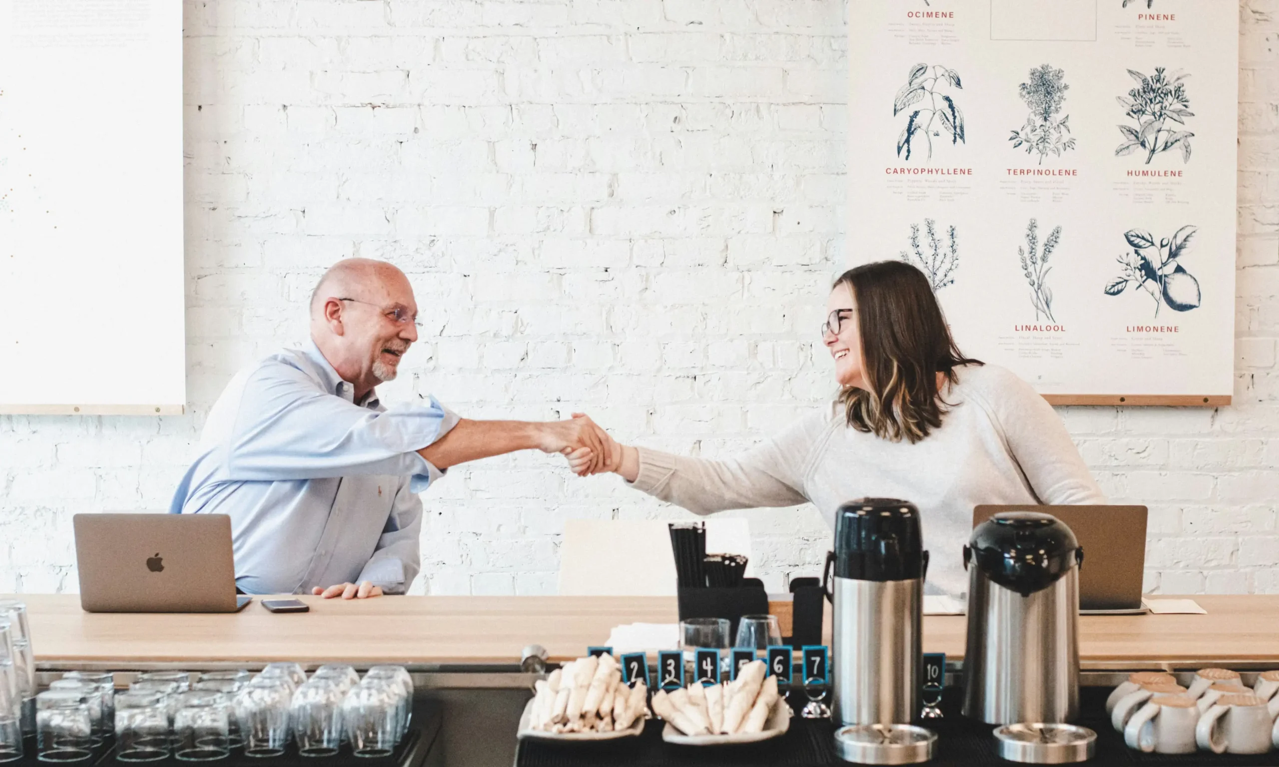 Two people smiling and shaking hands across a desk