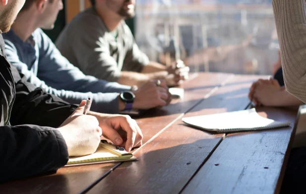 People writing notes together at a table in a meeting.