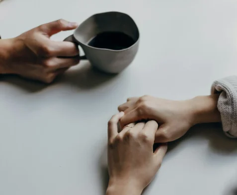 Two people holding hands beside a cup of coffee.